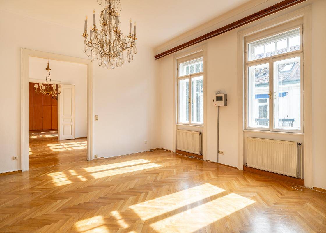 Lichtdurchflutetes Wohnzimmer mit elegantem Fischgrätparkett und großen Fenstern, die viel Helligkeit spenden.