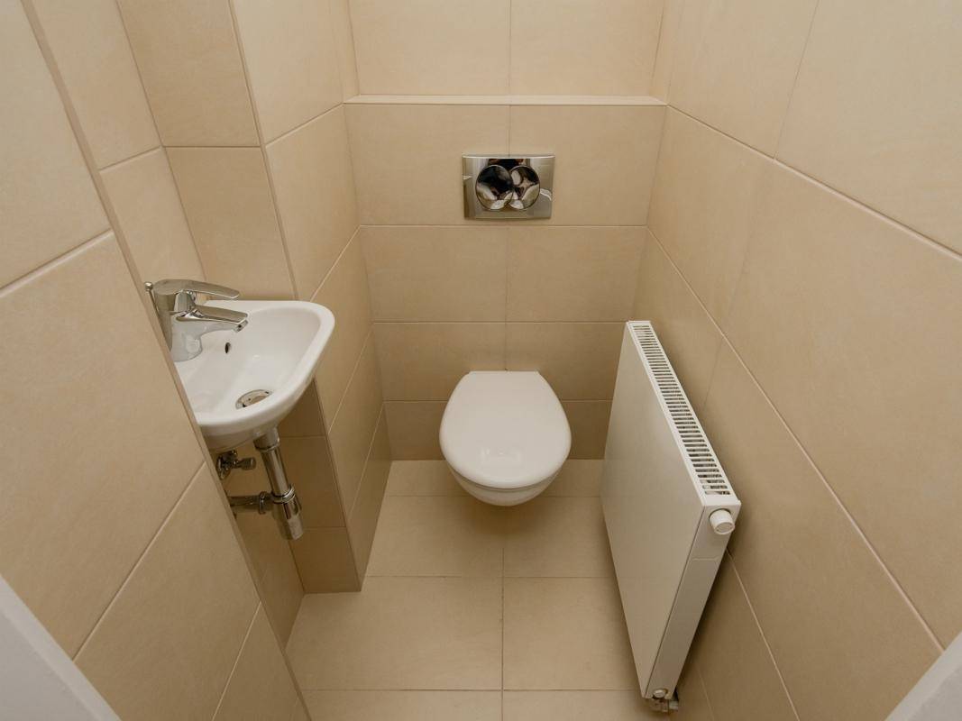 Kompaktes Gäste-WC mit beigefarbenen Fliesen, wandhängendem WC und kleinem Waschbecken.