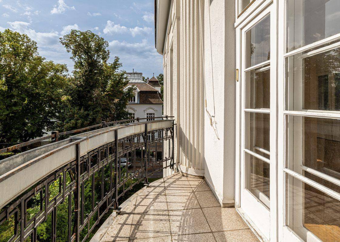Langer Balkon mit Fliesenboden und schmiedeeisernem Geländer, bietet einen Blick ins Grüne.