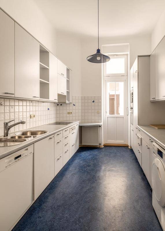 Funktionale Küche mit weißen Schränken, blauer Boden und Zugang zu einem kleinen Balkon.