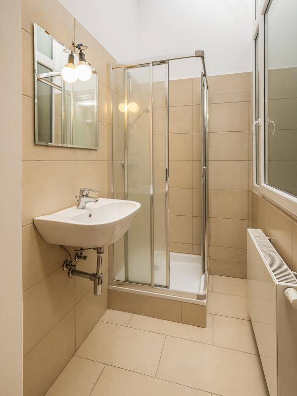 Modernes Badezimmer mit beigefarbenen Fliesen, Duschkabine und Fenster für natürliche Belüftung.