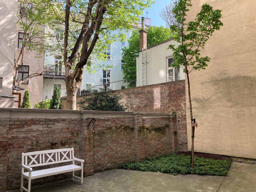Ruhiger Innenhof mit Sitzbank, Bäumen und Backsteinmauern, ideal zum Entspannen.