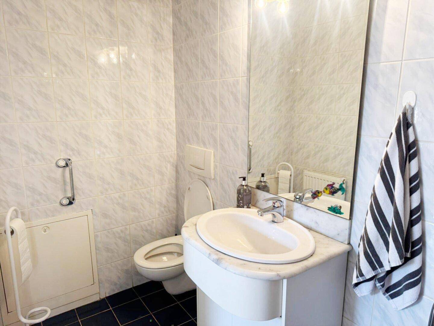 Badezimmer mit hellen Fliesen, Waschbecken, Toilette und Wandspiegel.