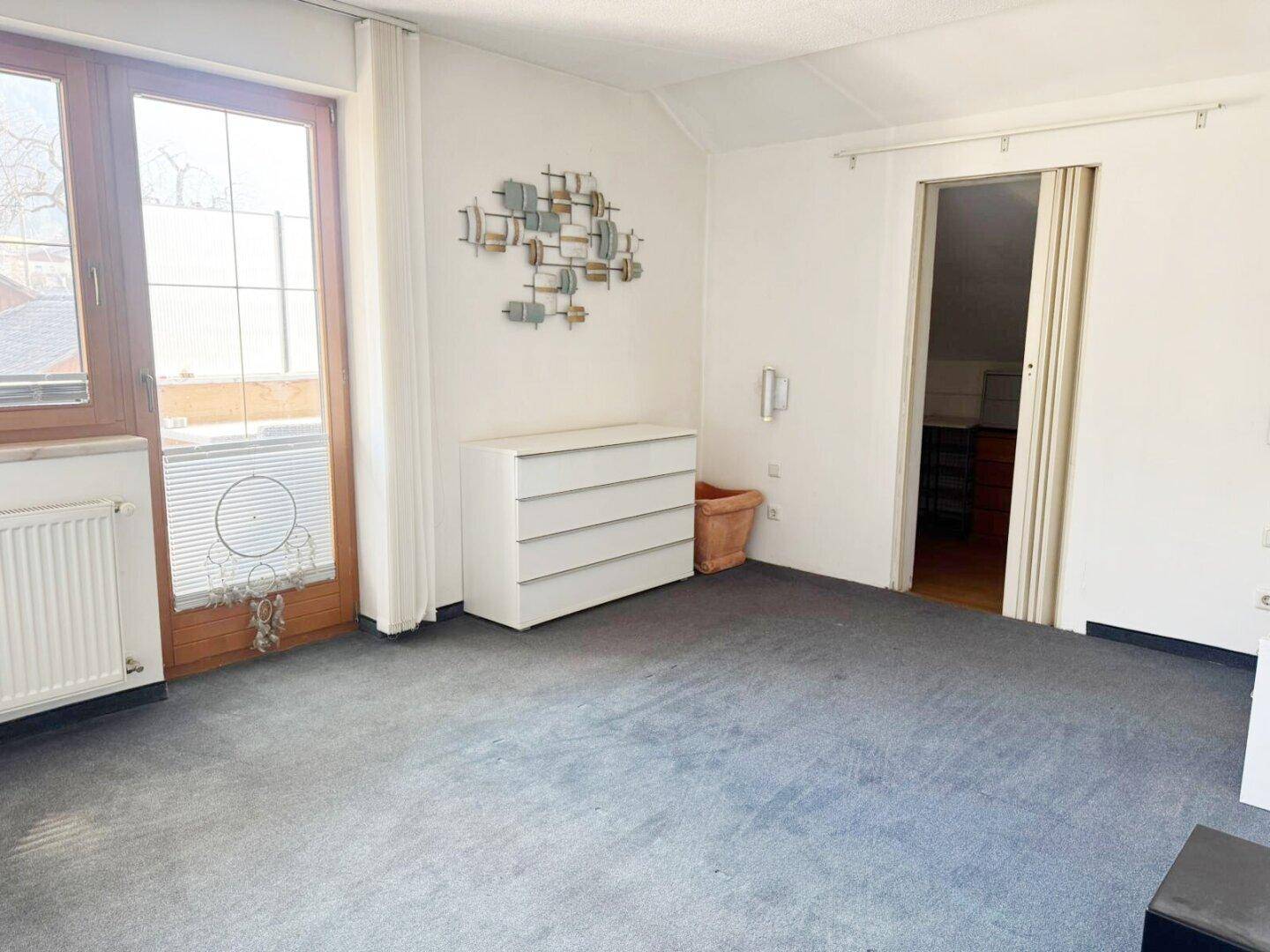 Raum mit Teppichboden und Zugang zu einem Balkon, ausgestattet mit einem Sideboard.
