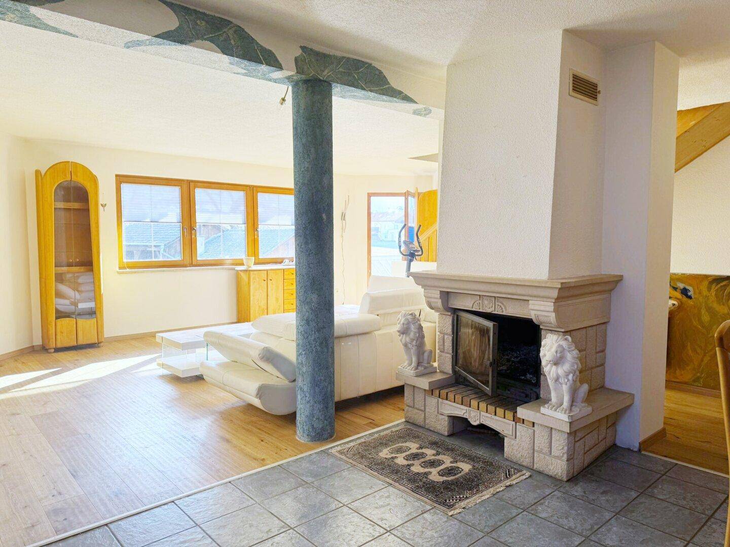 Geräumiges Wohnzimmer mit Kamin, Holzboden und Säulen als dekorative Elemente.