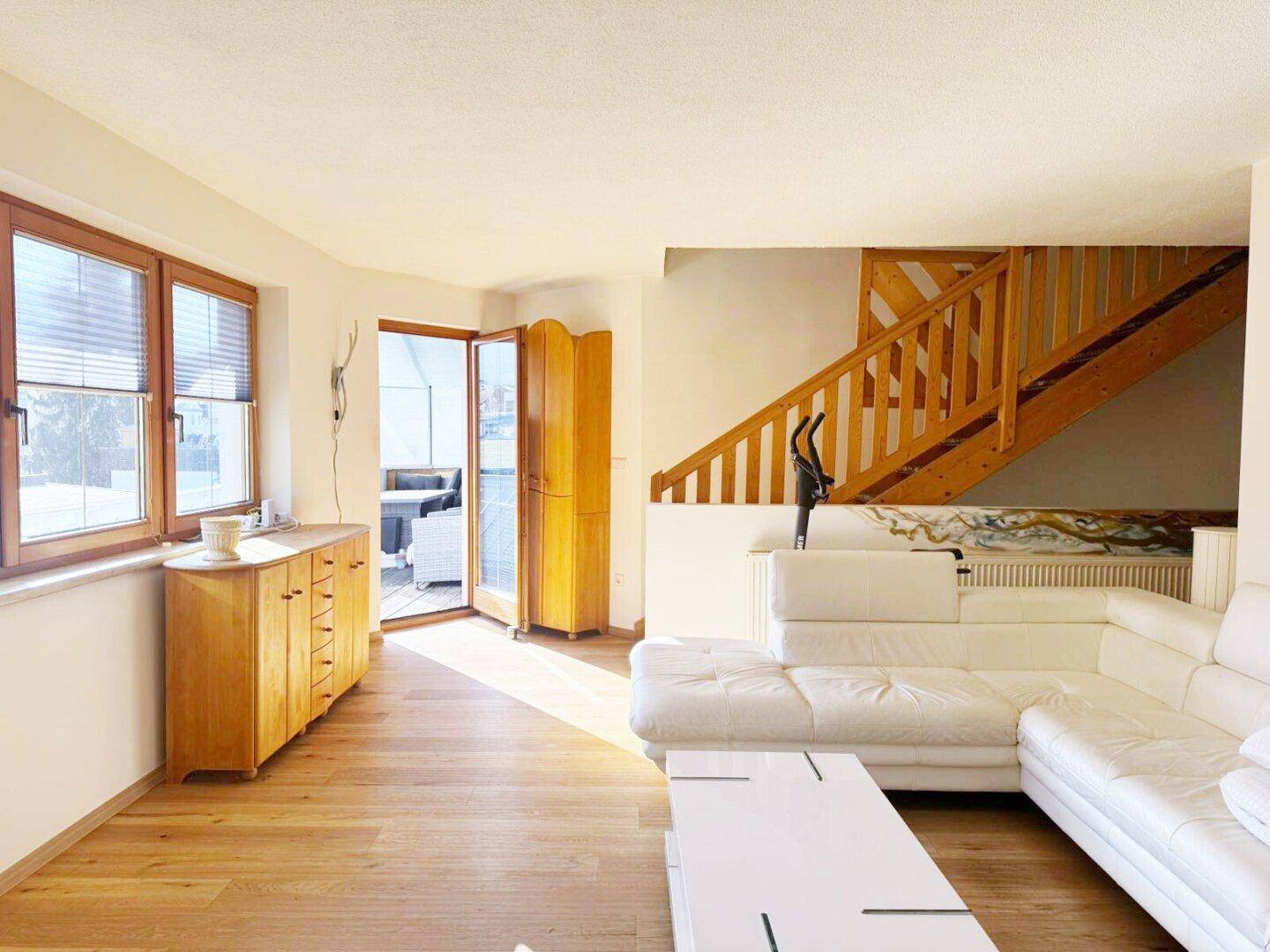 Helles Wohnzimmer mit Holzboden, weißem Sofa und Holztreppe zum Obergeschoss.