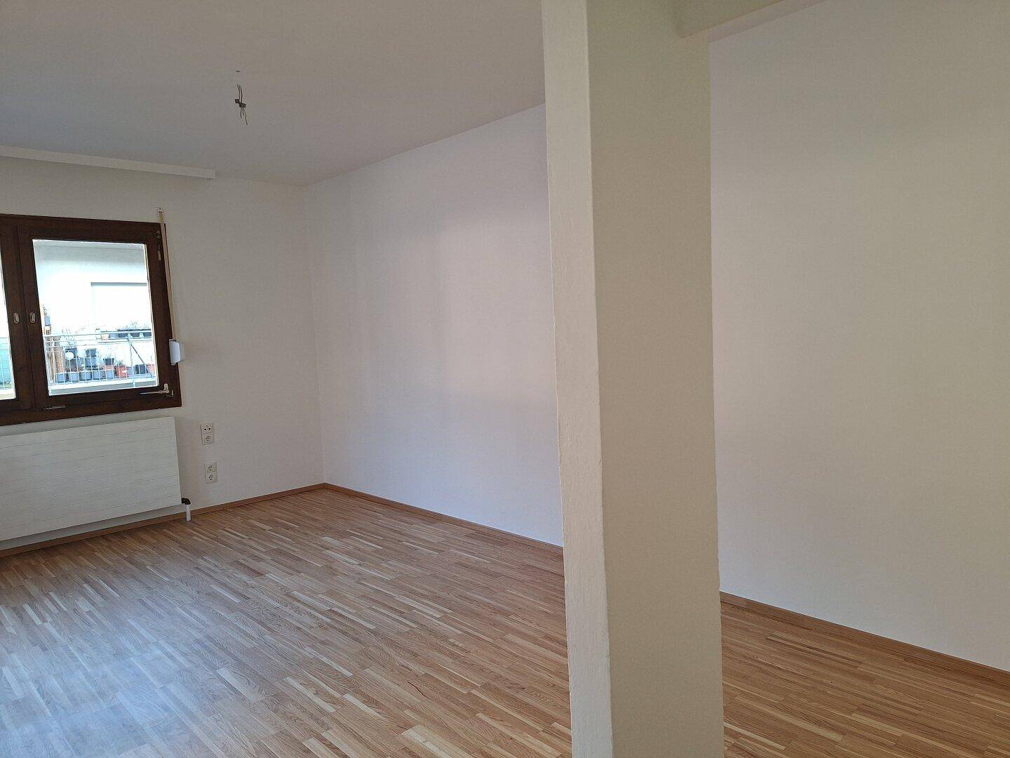 Geräumiger, unmöblierter Wohnbereich mit weiß gestrichenen Wänden und einem Säulenelement.