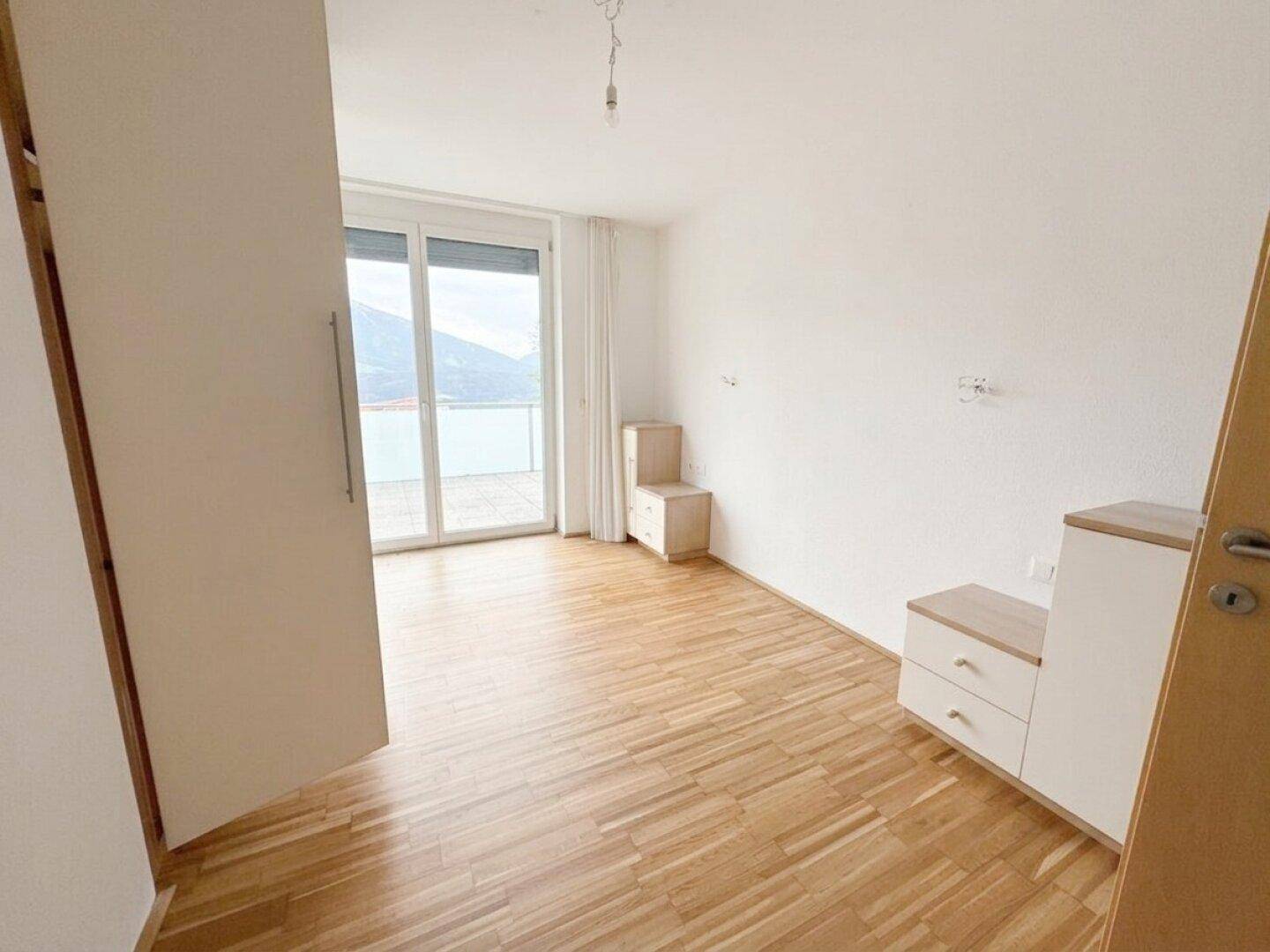 Schlafzimmer mit Parkettboden, Zugang zum Balkon und Blick auf die umliegende Landschaft.