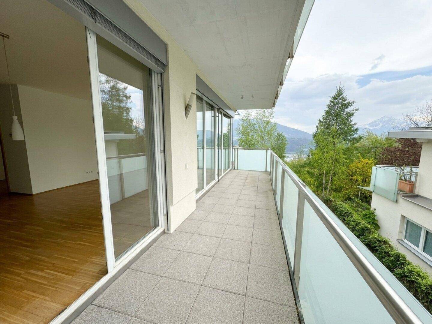 Langer Balkon mit Fliesenboden, Glasgeländer und weitem Blick auf die umliegende Berglandschaft.