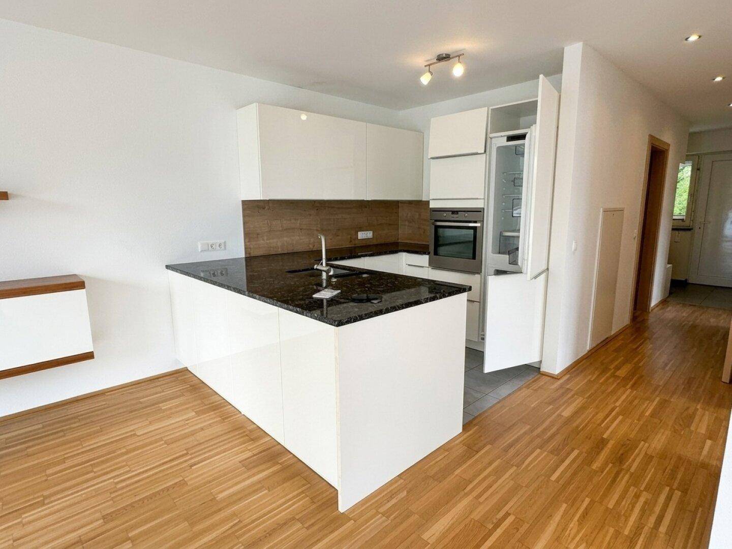 Moderne Einbauküche mit weißen Hochglanzfronten, schwarzer Granitarbeitsplatte und integrierten Geräten.