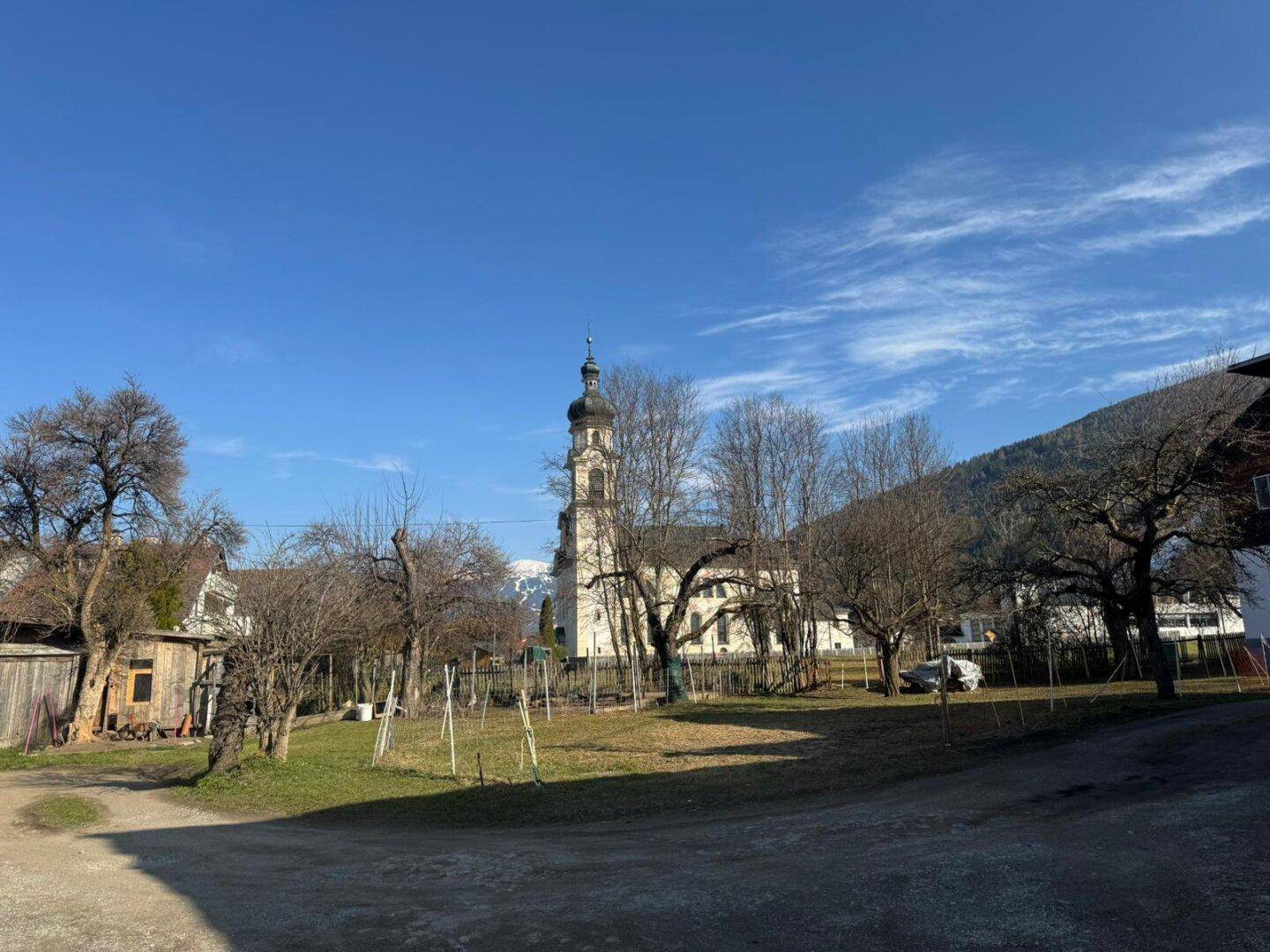 Weitläufiger Blick auf eine Kirche mit Zwiebelturm und schneebedeckte Berge im Hintergrund.