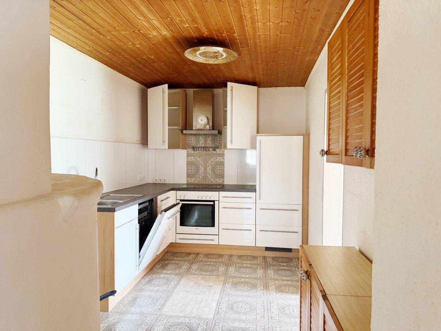 Helle Küche mit weißen Schränken, Holzdecke, Fliesenboden und integrierten Geräten.