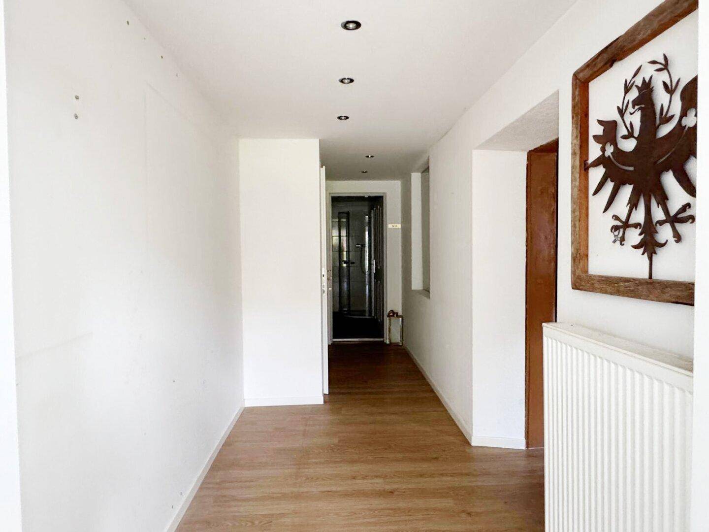 Heller Flur mit Holzfußboden, weißen Wänden und Einbaustrahlern in der Decke.