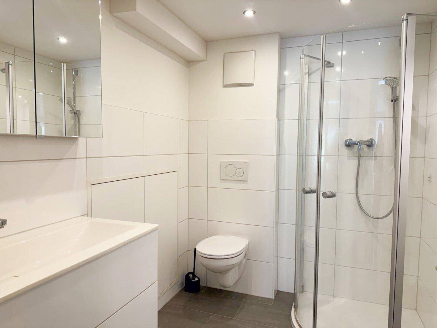 Modernes Badezimmer mit Duschkabine, Wand-WC, Waschbecken und weißen Fliesen.