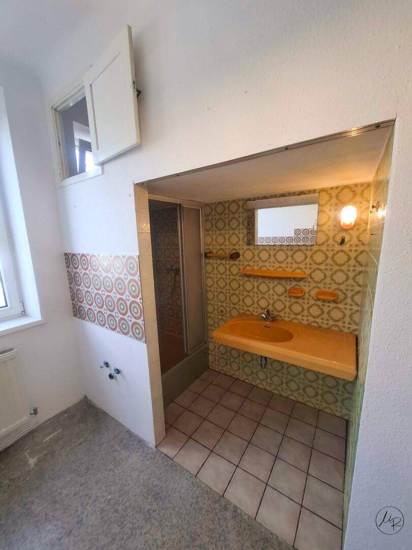 Badezimmer mit Duschkabine, Waschbecken und auffälligen Retro-Fliesen, bereit zur Renovierung.