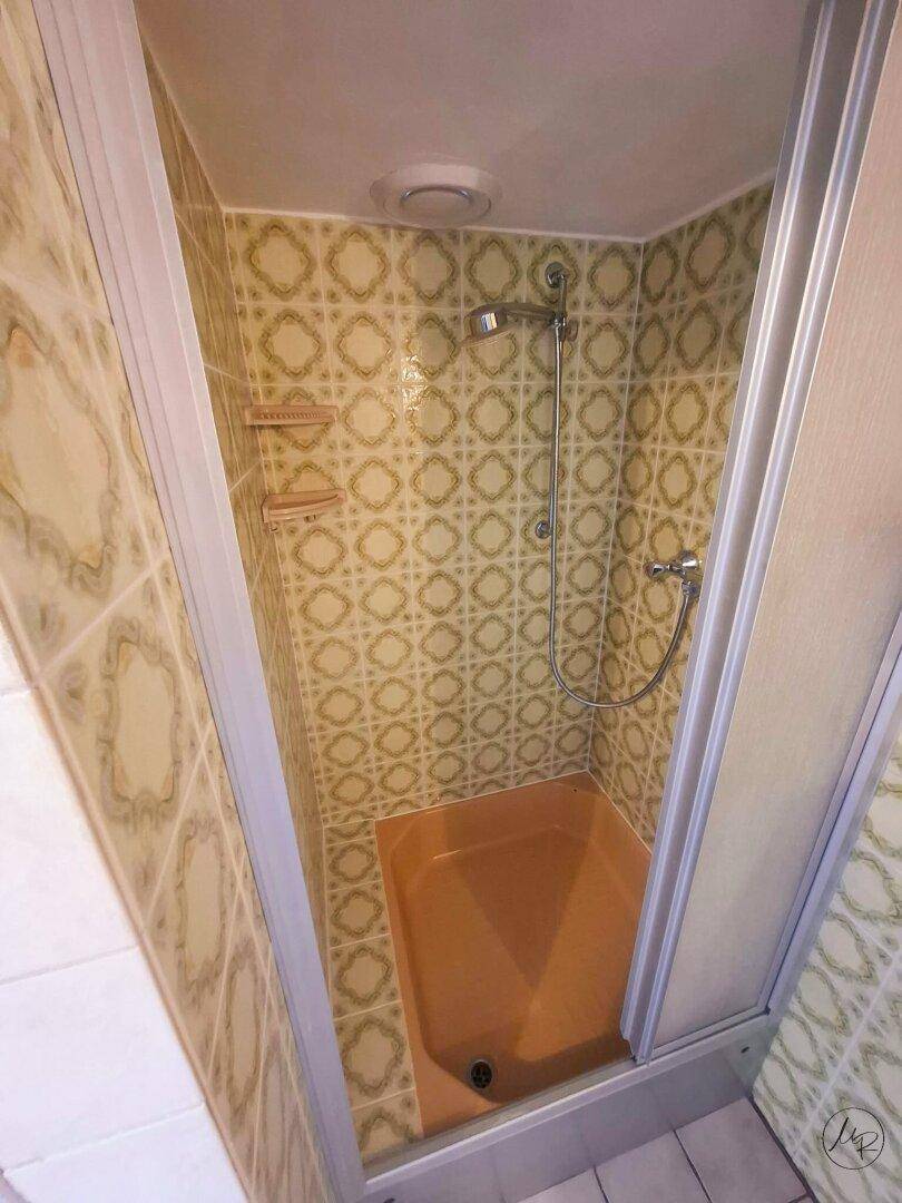 Duschkabine mit Retro-Fliesen und orangefarbener Duschwanne, typisch für ältere Badezimmer.
