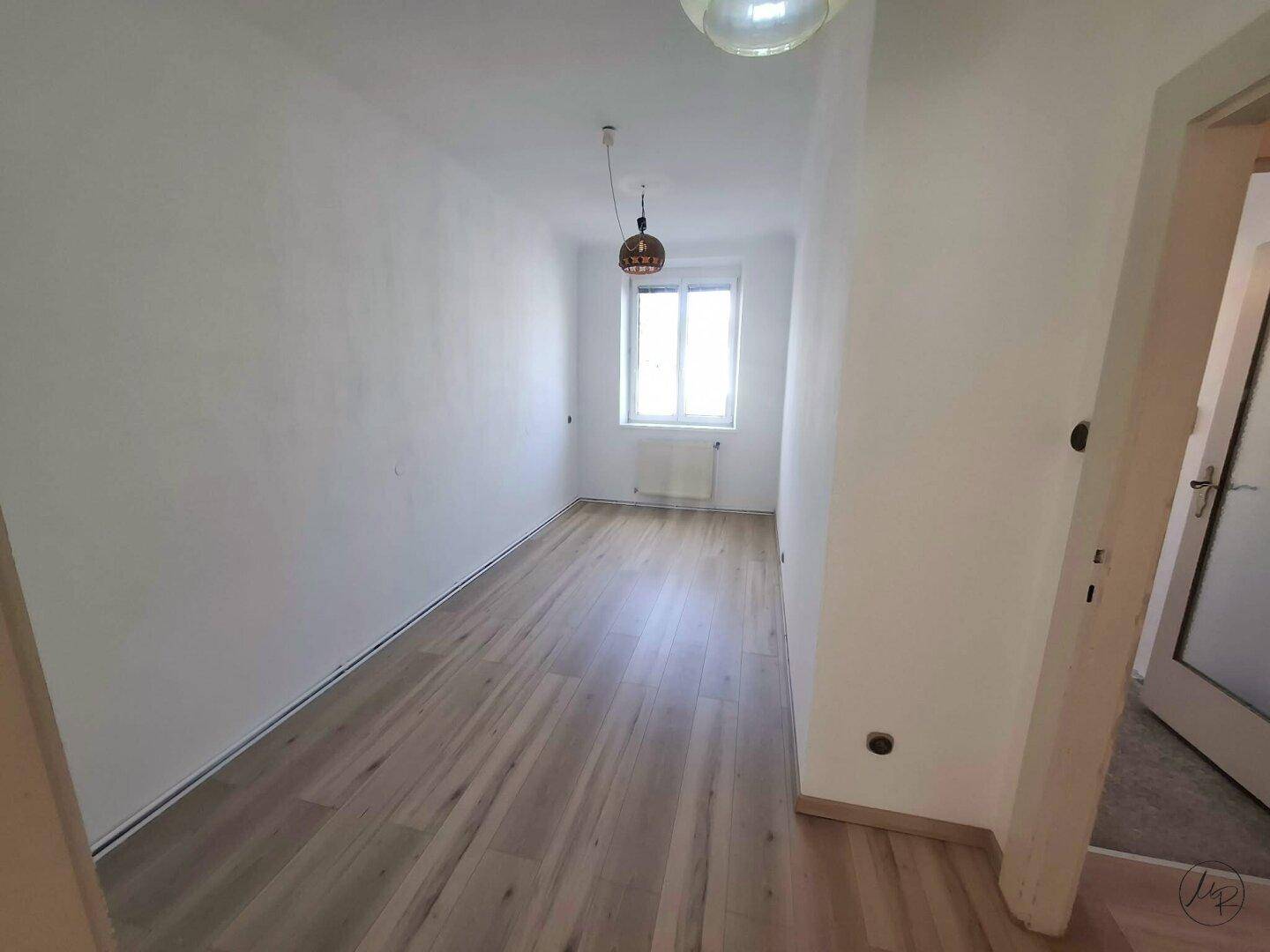 Helles, leeres Schlafzimmer mit Laminatboden und weißen Wänden, bietet vielseitige Nutzungsmöglichkeiten.