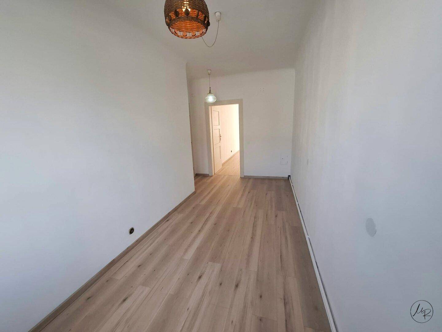 Schmaler, heller Flur mit neuem Laminatboden und weißen Wänden, der zu weiteren Räumen führt.