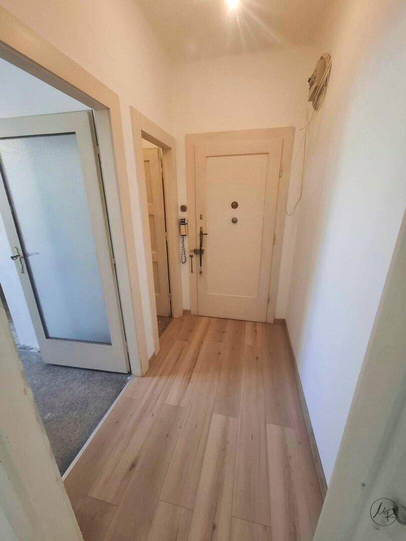 Heller Eingangsbereich mit Laminatboden und weißen Wänden, der zu verschiedenen Zimmern führt.