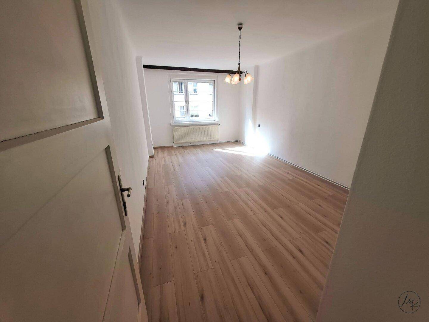 Geräumiger, heller Wohnraum mit neuem Laminatboden und weißen Wänden, ideal für individuelle Einrichtung.