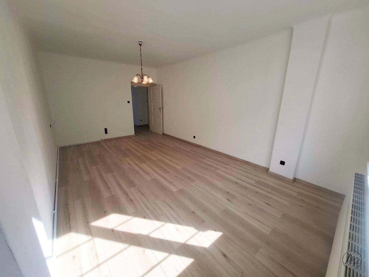 Heller, leerer Raum mit neuem Laminatboden und weißen Wänden, bereit zur individuellen Gestaltung.