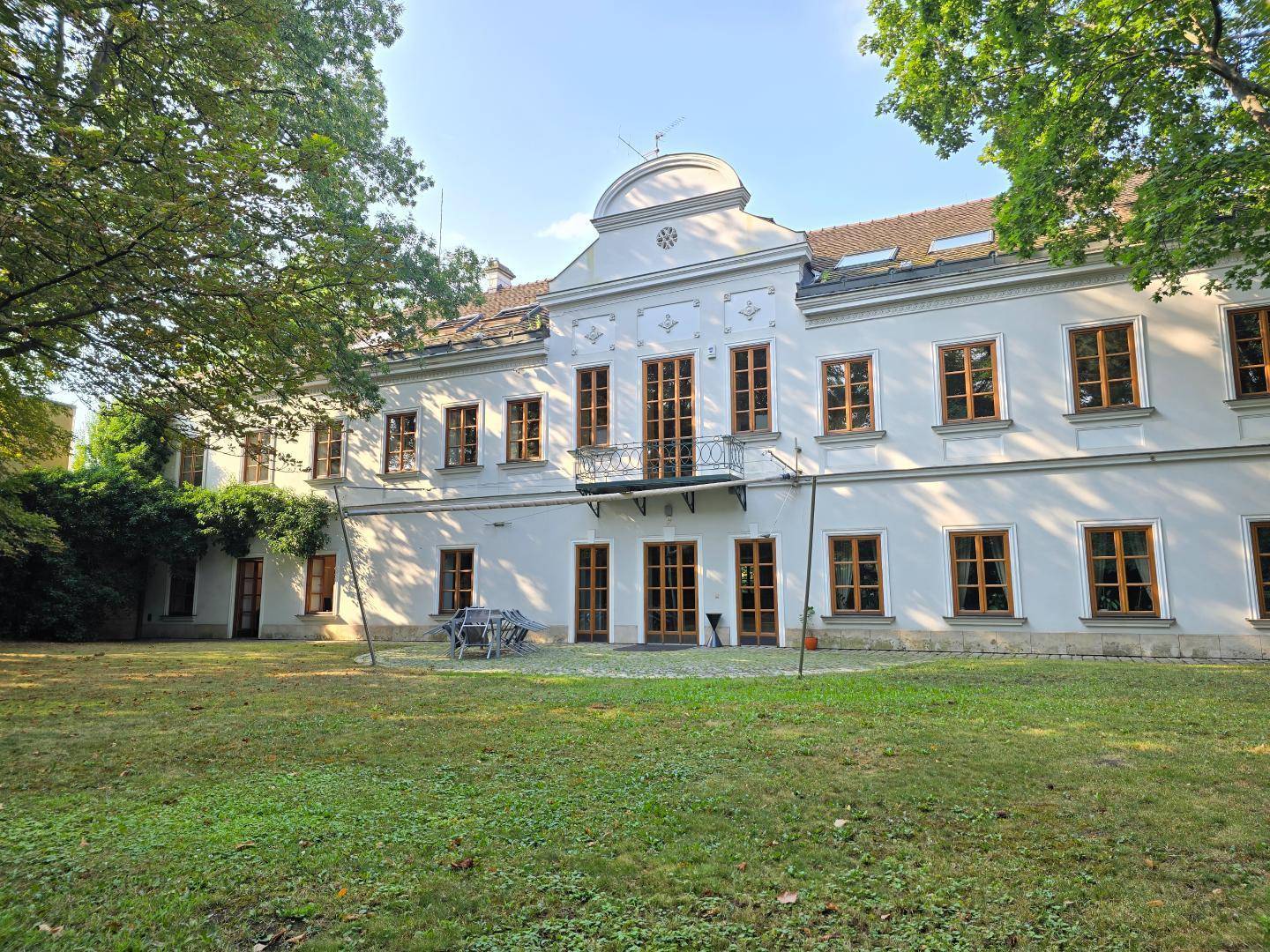 Historisches weißes Gebäude mit klassischer Architektur, umgeben von einem weitläufigen grünen Gartenbereich.