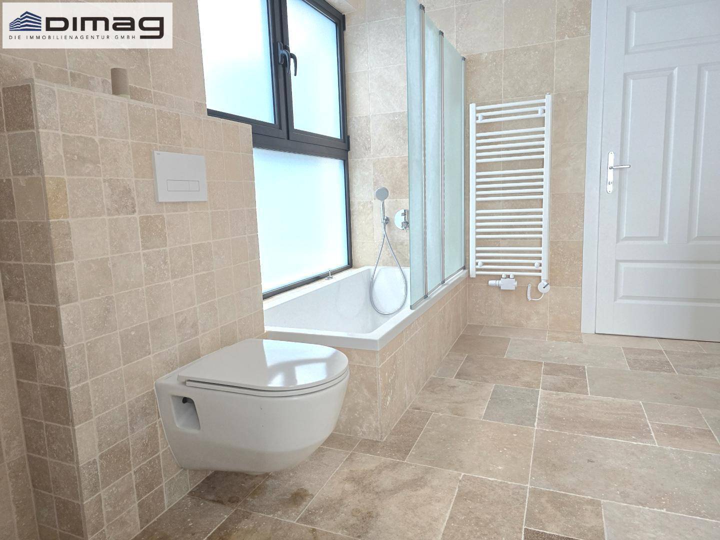 Helles Badezimmer mit Badewanne, wandhängendem WC, Fenster und beheiztem Handtuchhalter.