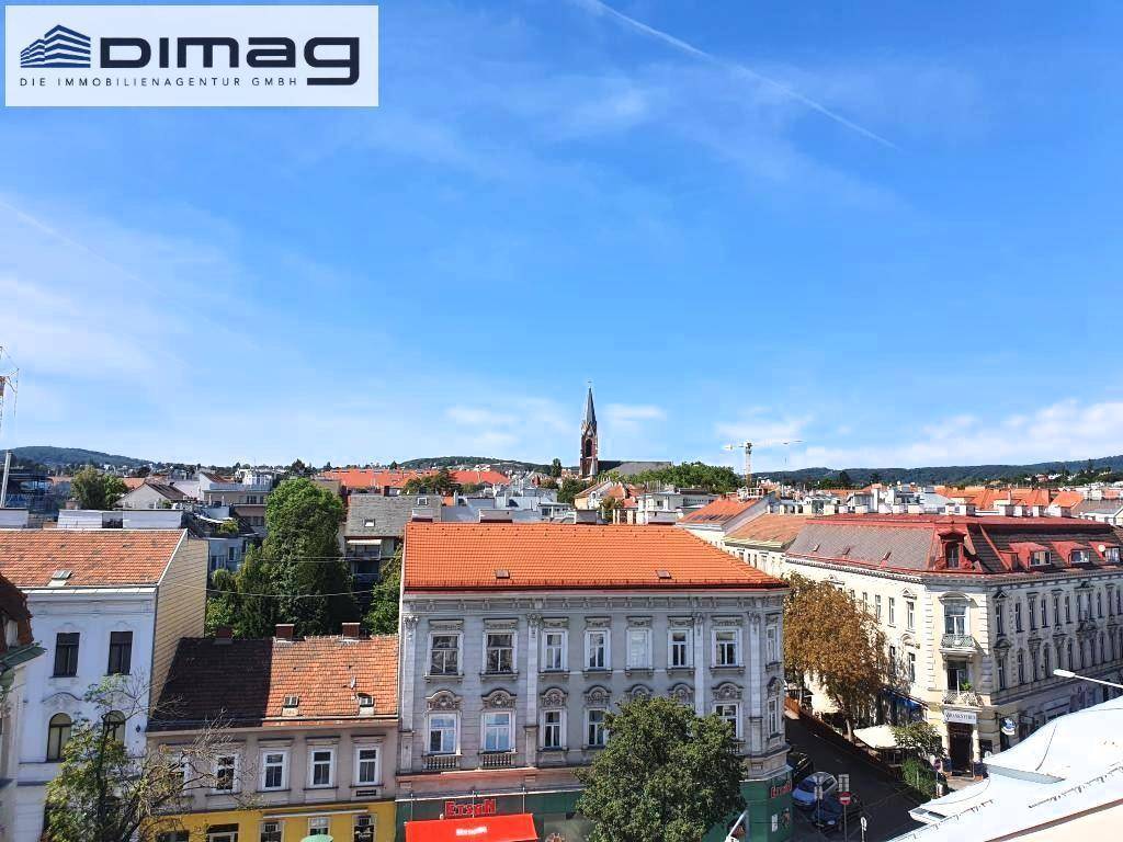 Weitläufiger Ausblick auf die Dächer der Stadt, umgeben von grünen Hügeln und einem Kirchturm.
