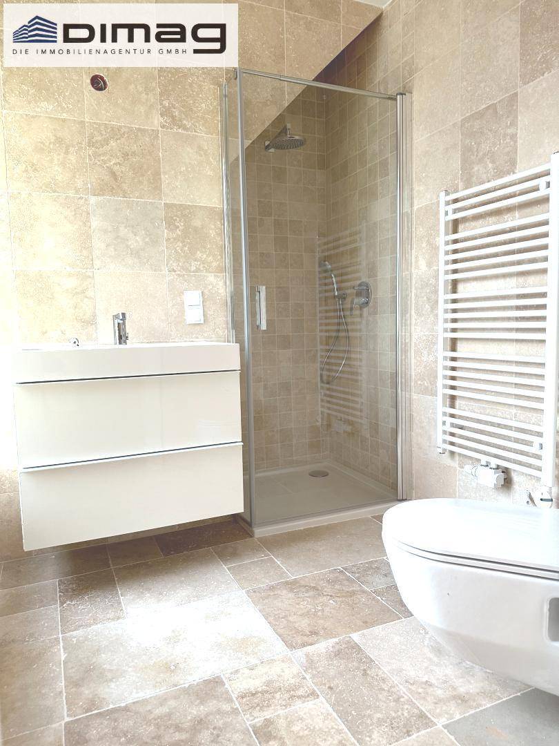 Modernes Badezimmer mit beigefarbenen Fliesen, Waschtisch, Duschkabine und beheiztem Handtuchhalter.
