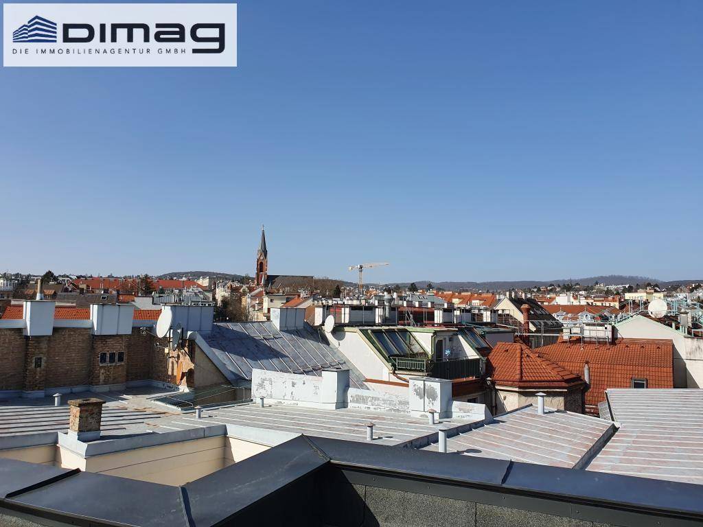 Dachlandschaft der Stadt mit verschiedenen Gebäuden und einem Kirchturm im Hintergrund.