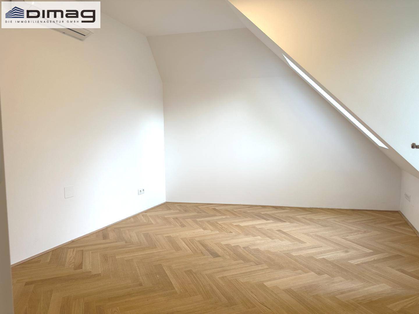 Helles Zimmer mit Fischgrätparkett, Dachschräge und einem Dachschrägenfenster.