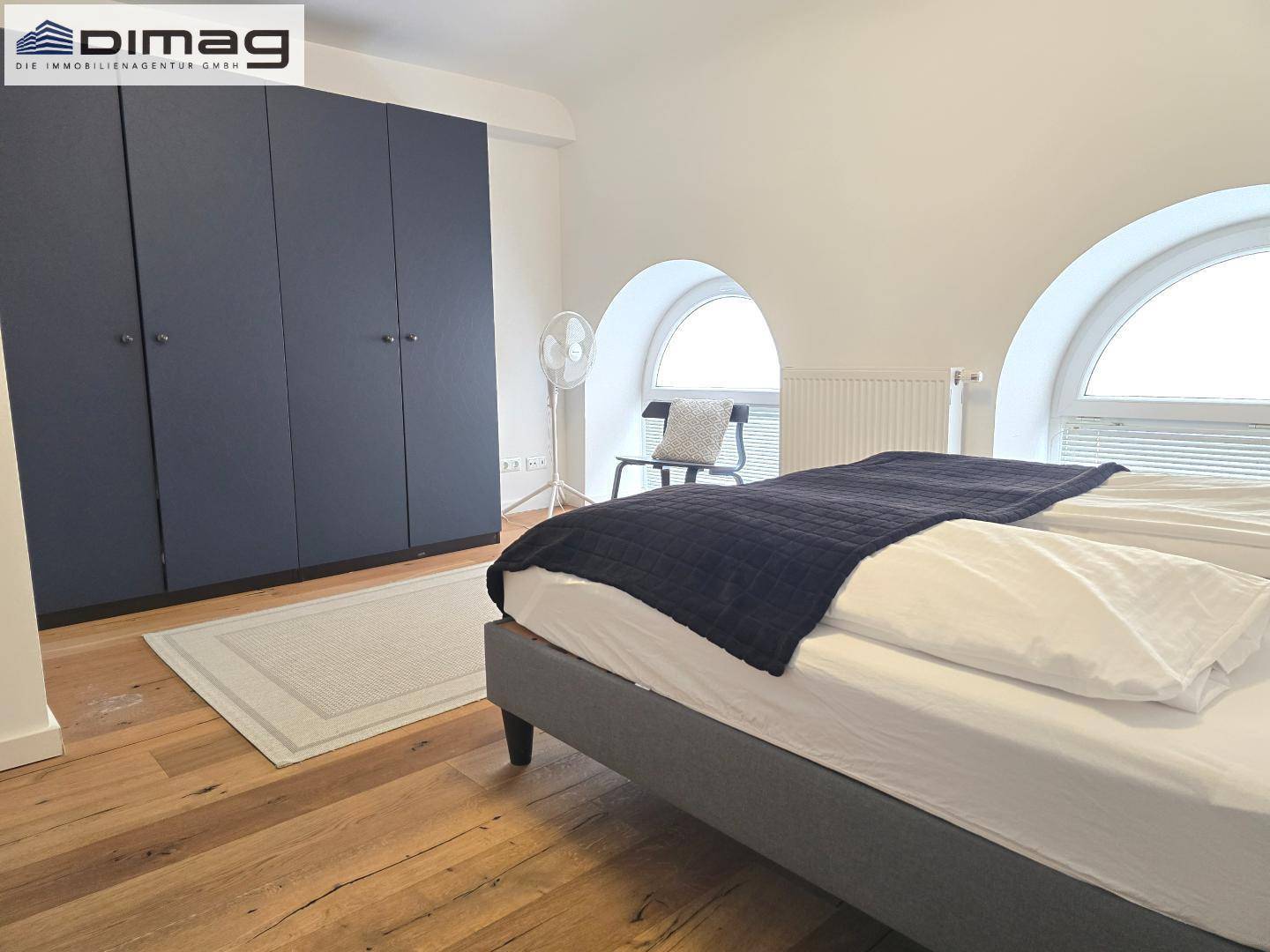 Geräumiges Schlafzimmer mit Holzboden, großem Kleiderschrank und Rundbogenfenstern.