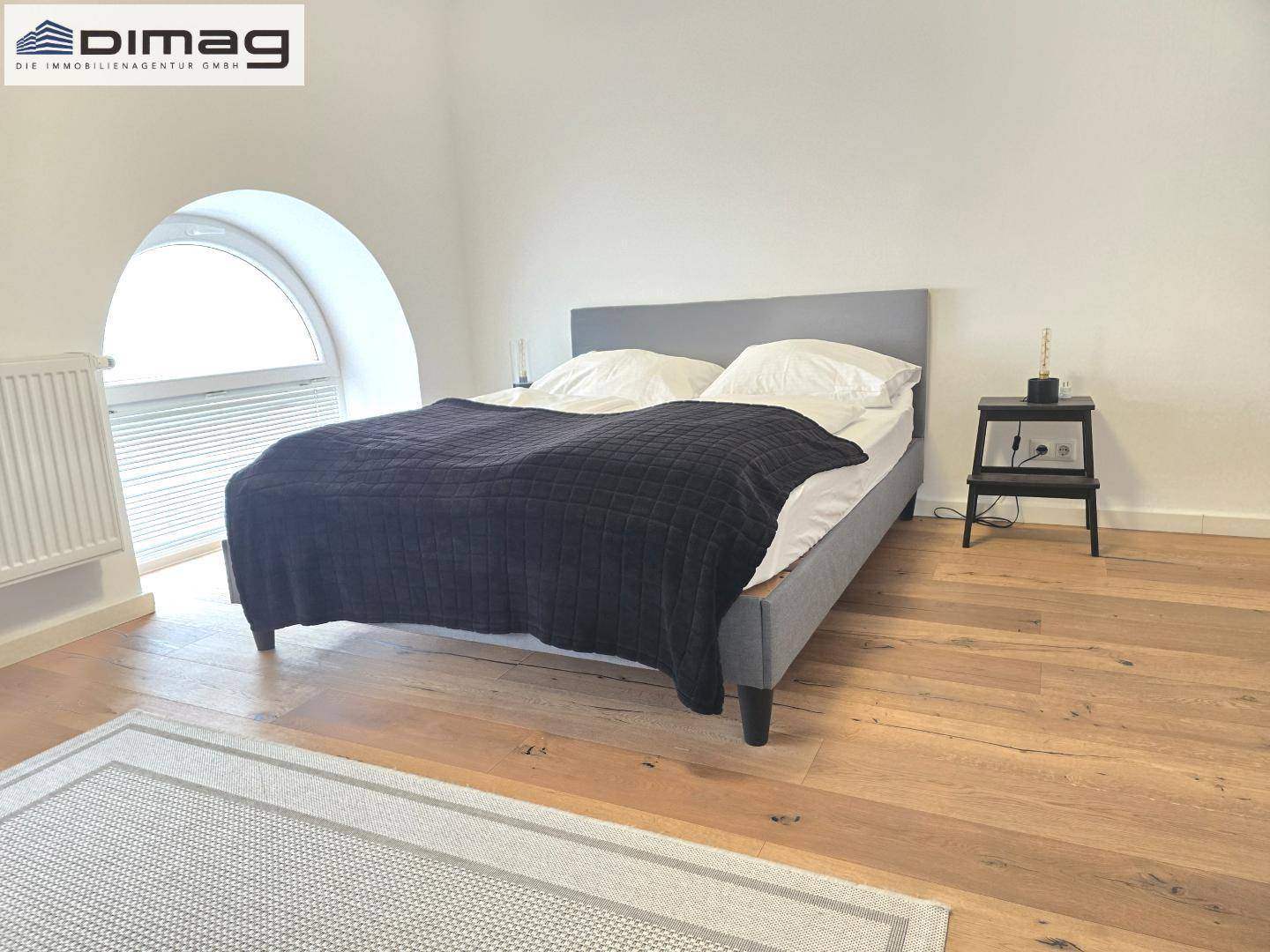 Schlafzimmer mit Holzboden, Doppelbett und einem großen Rundbogenfenster.
