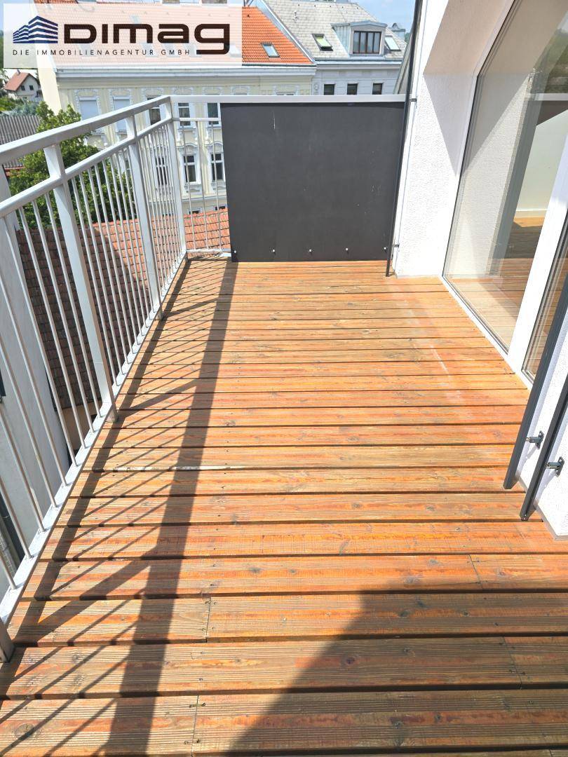Sonniger Balkon mit Holzboden und Metallgeländer, bietet Blick auf die Umgebung.