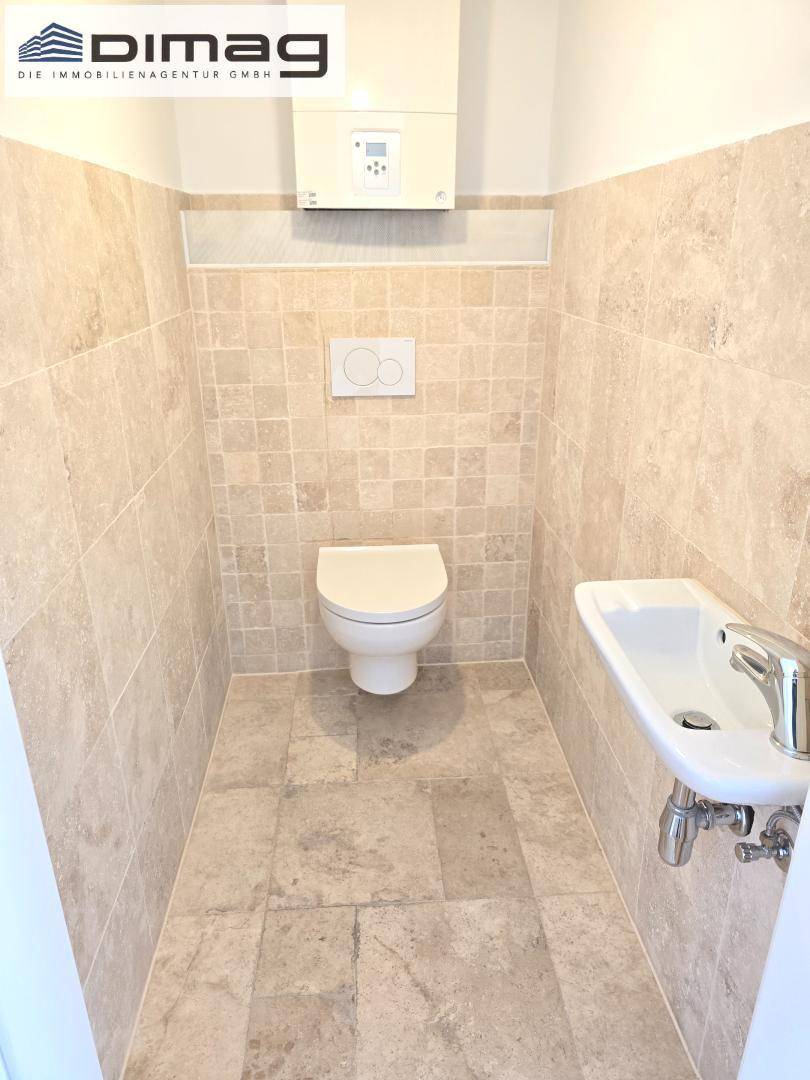 Kleines Gäste-WC mit Wand-WC, Waschbecken und beigefarbenen Fliesen.