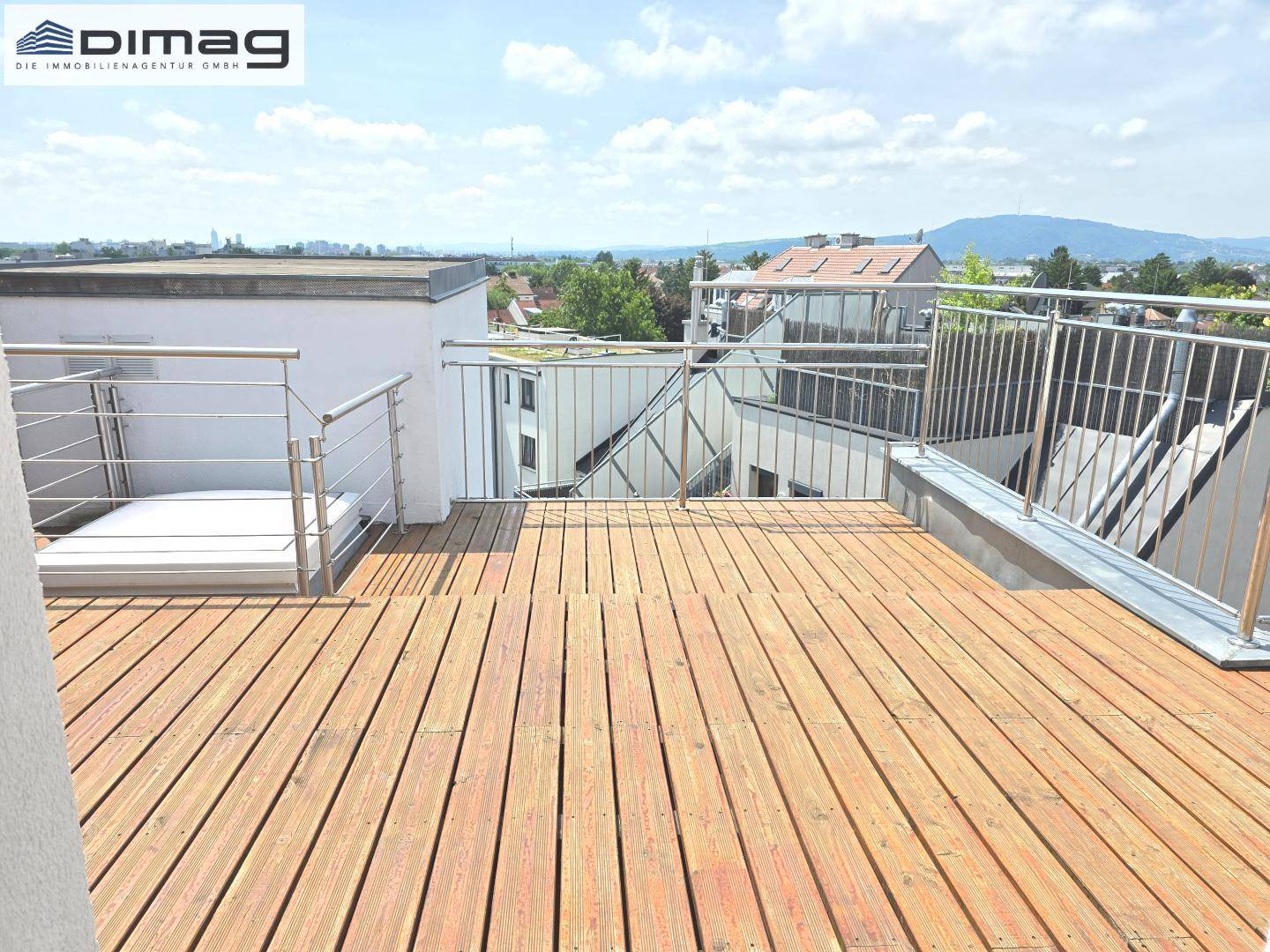 Sonniger Außenbereich auf der Dachterrasse mit Holzboden und Panoramablick.