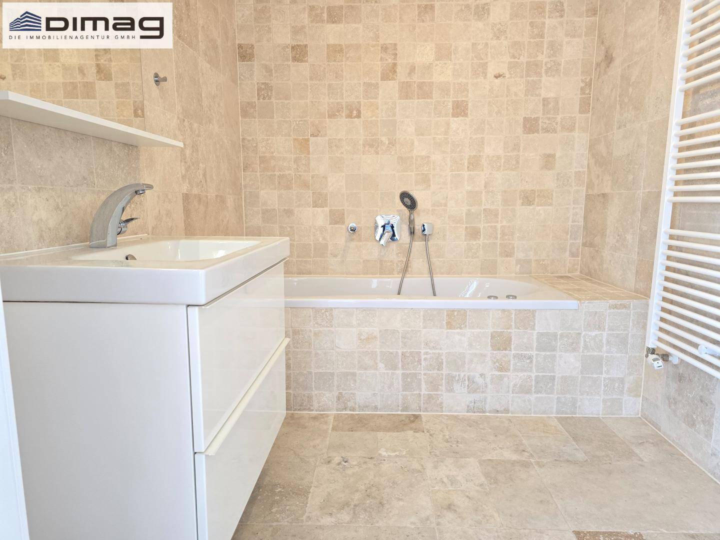 Modernes Badezimmer mit Badewanne, Waschbecken und beigefarbenen Fliesen.