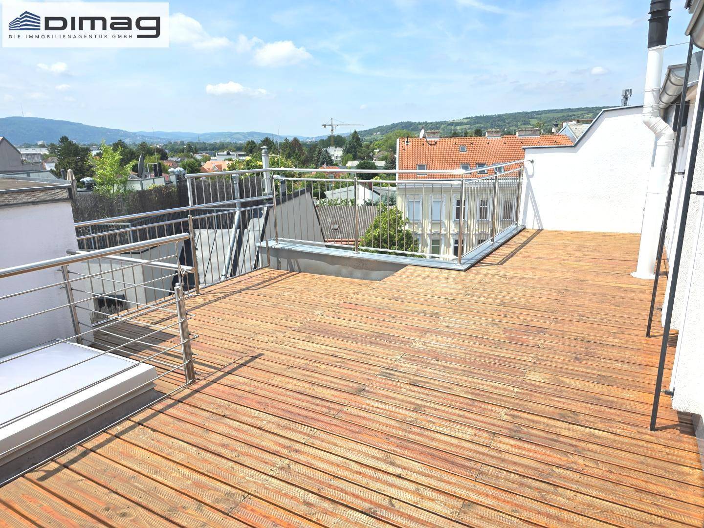 Geräumige Dachterrasse mit Holzboden und weitem Blick über die Stadt und Berge.