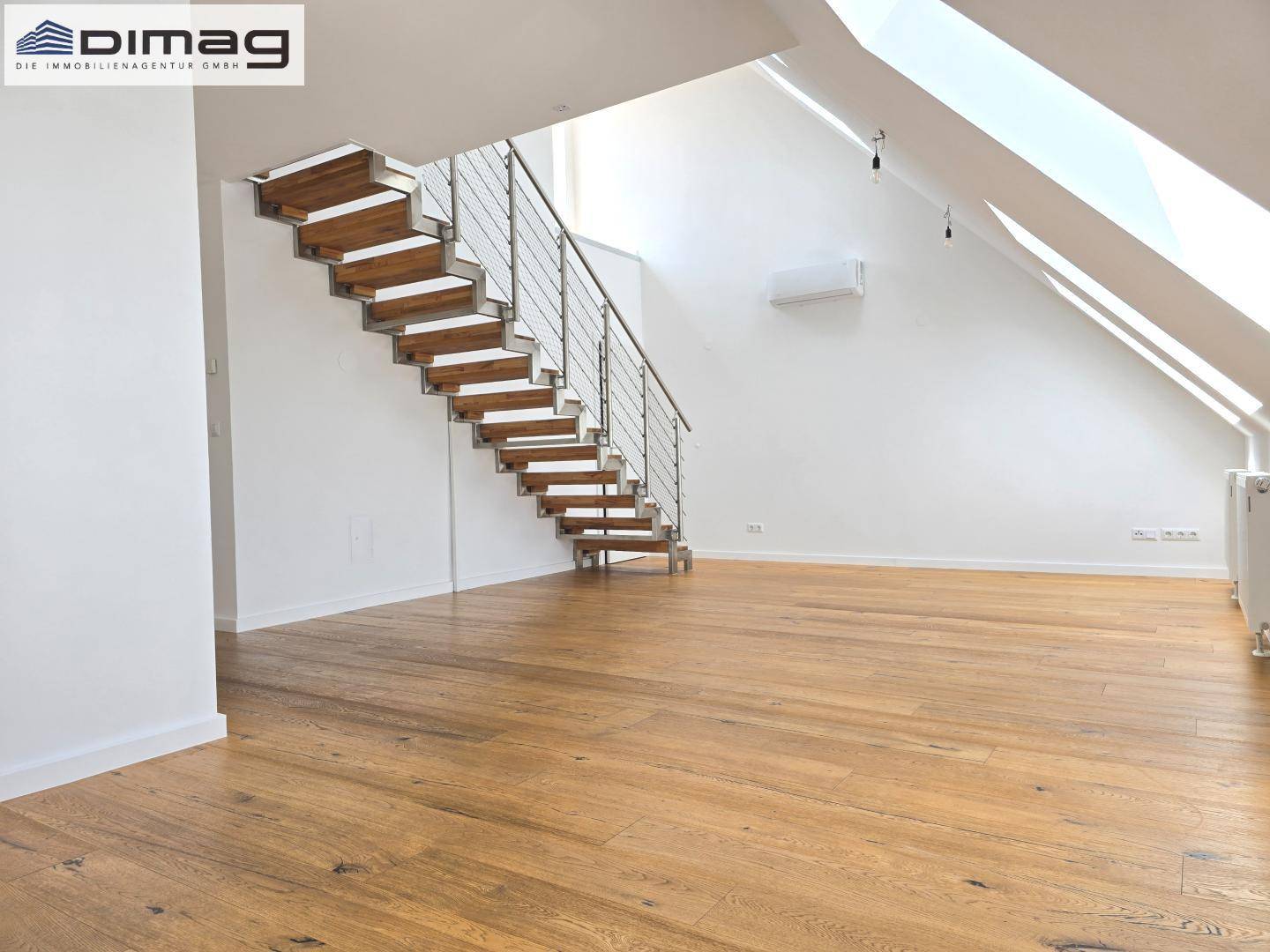 Heller Wohnbereich mit moderner Holztreppe und viel Tageslicht durch Dachfenster.