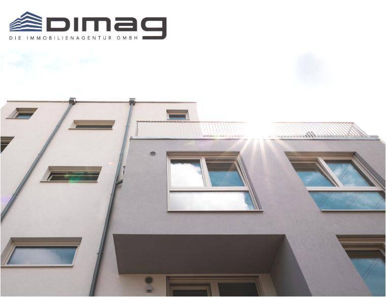 Sonnenlicht fällt auf die moderne Fassade eines Gebäudes mit großen Fenstern und einem Balkon.
