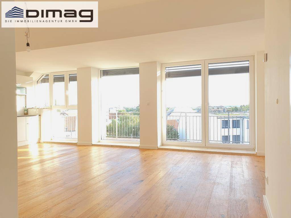 Lichtdurchfluteter Wohnbereich mit Holzboden und weitem Blick über die Dächer der Stadt durch große Fenster.