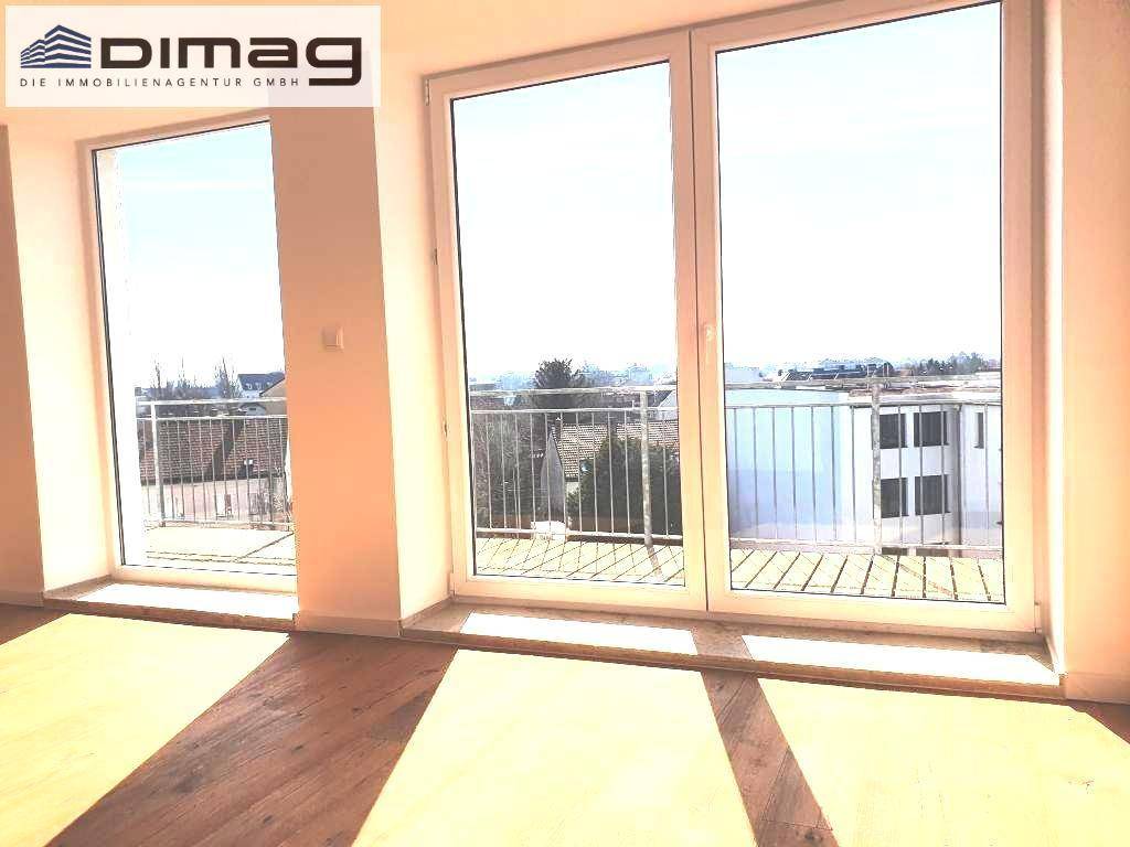 Große Fensterfront im Wohnbereich mit Zugang zu einem Balkon und Blick auf die umliegenden Gebäude.