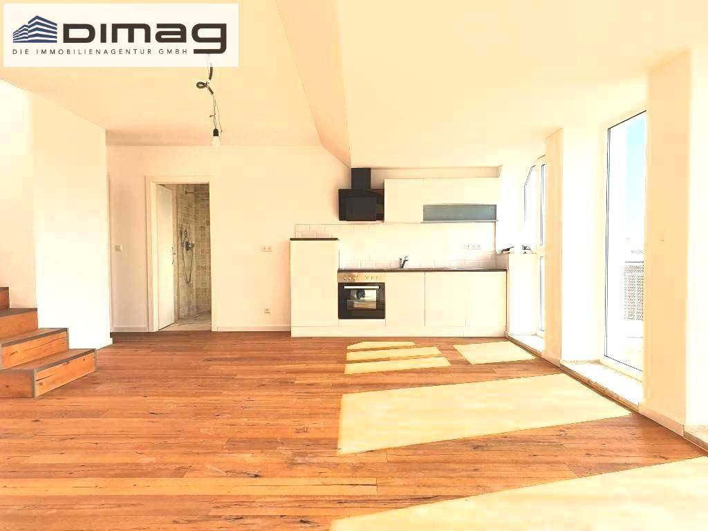 Offener Wohnbereich mit Holzboden, integrierter Küche und einer Holztreppe, die in eine weitere Etage führt.