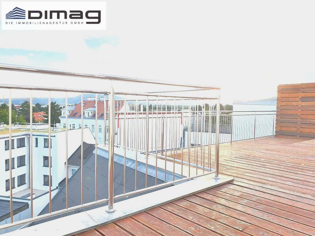 Dachterrasse mit Holzbelag und Metallgeländer, die einen Blick auf die Dächer der Nachbargebäude bietet.