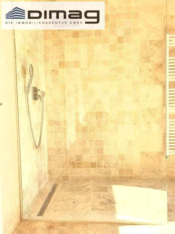 Geräumige begehbare Dusche mit Glasabtrennung, beigefarbenen Fliesen und einem beheizten Handtuchhalter.