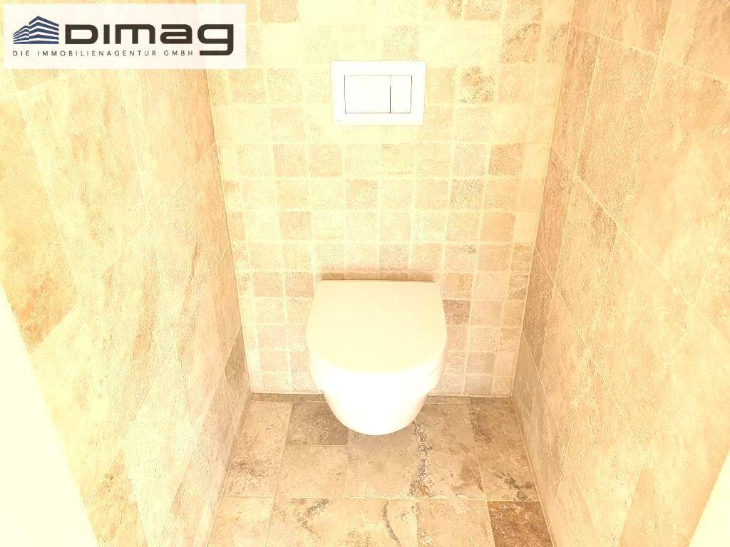 Separates WC mit beigefarbenen Fliesen und einer wandhängenden Toilette.
