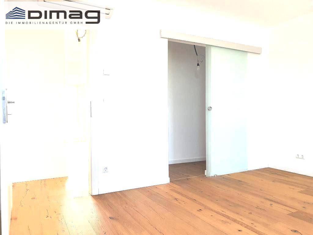 Innenraum mit Holzboden und einer modernen Glasschiebetür, die zu einem weiteren Bereich führt.
