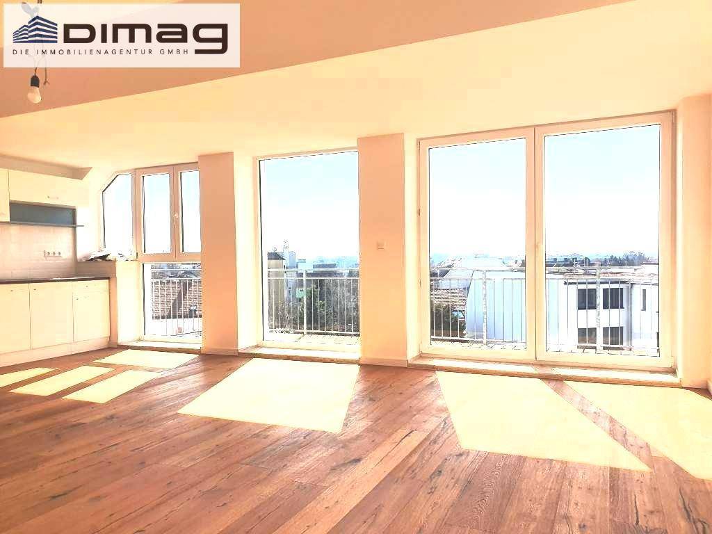 Sonniger Wohnbereich mit Holzboden und Panoramafenstern, die einen weiten Blick über die Umgebung bieten.