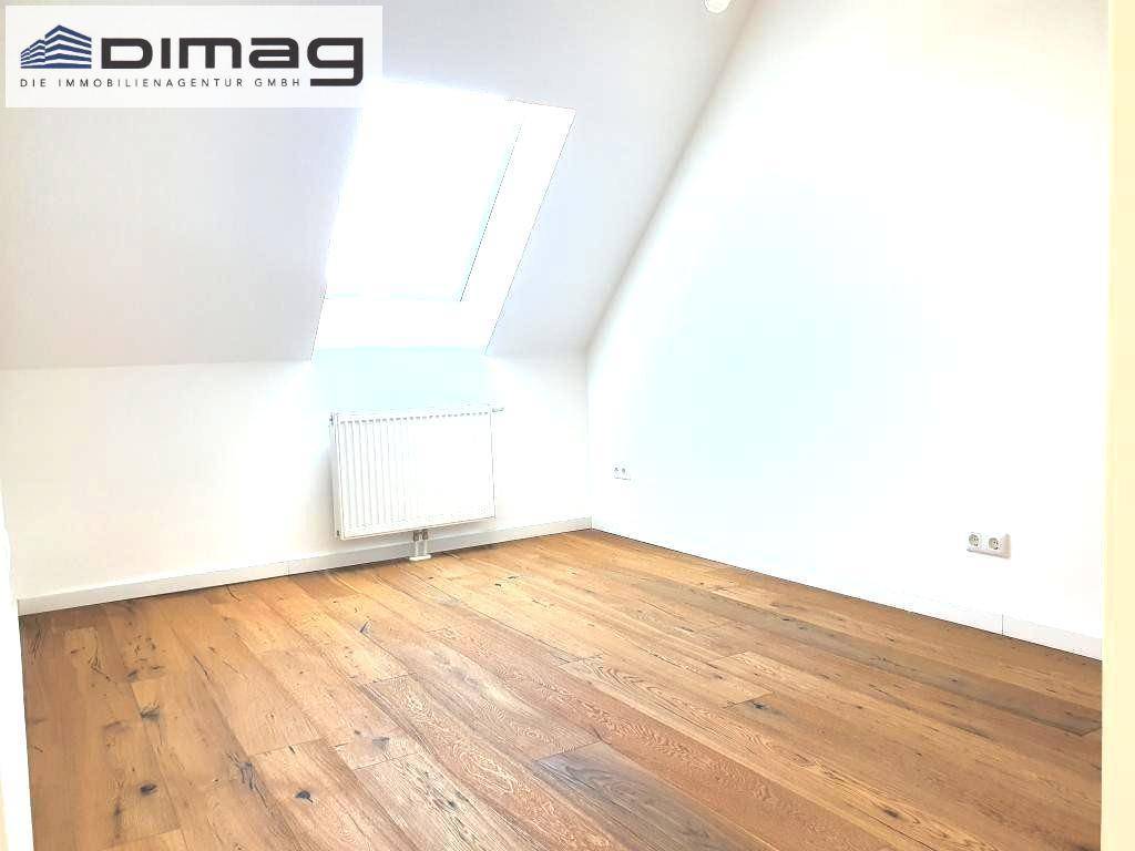 Helles Schlafzimmer im Dachgeschoss mit Holzboden, Dachschräge und einem Dachfenster für natürliches Licht.