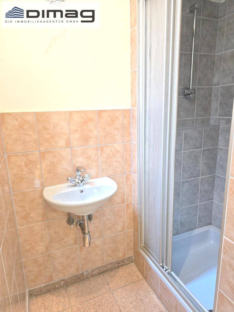 Badezimmer mit Waschbecken und Duschkabine, gefliesten Wänden und Boden.